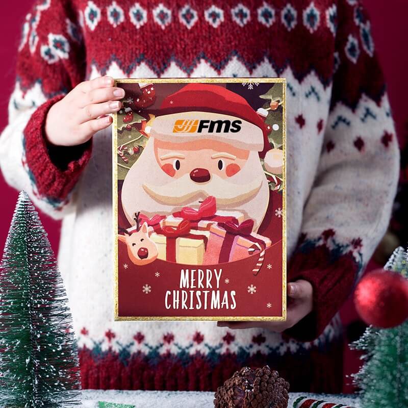 Christmas gift box with Santa Claus and FMS logo, held by a person in a festive sweater.